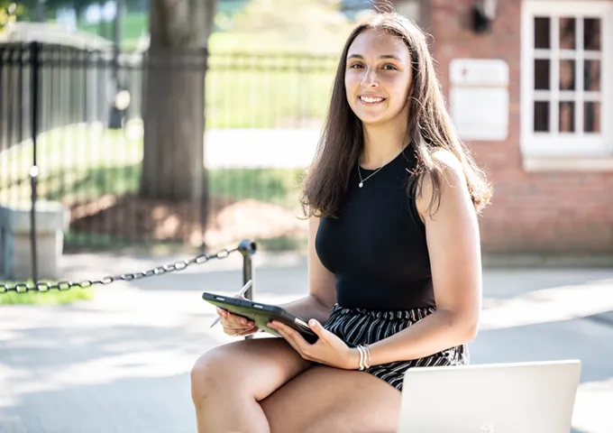 Female civilian student sitting on campus bench with her iPad.