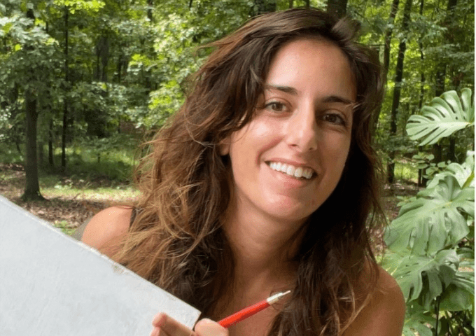 Female artist with pencil and sketchpad smiling at camera