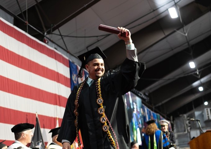 Norwich Graduate Crossing stage holding up diploma