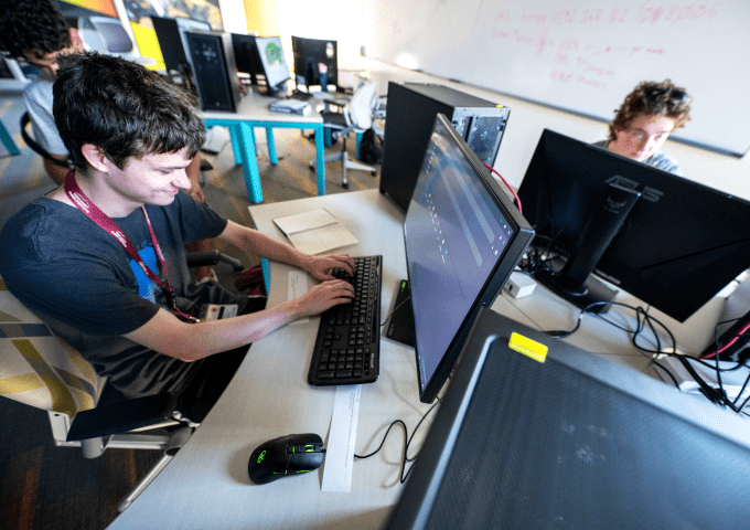 Student sits at desk surrounded by computer screens and working on computer project.