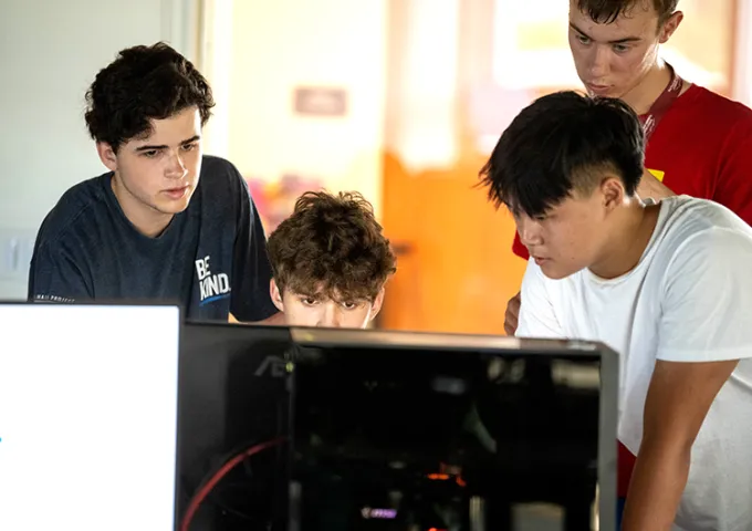 Four students standing around the computer screen, working together.