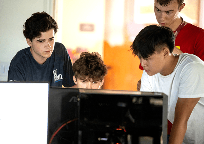 Four students standing around the computer screen, working together.
