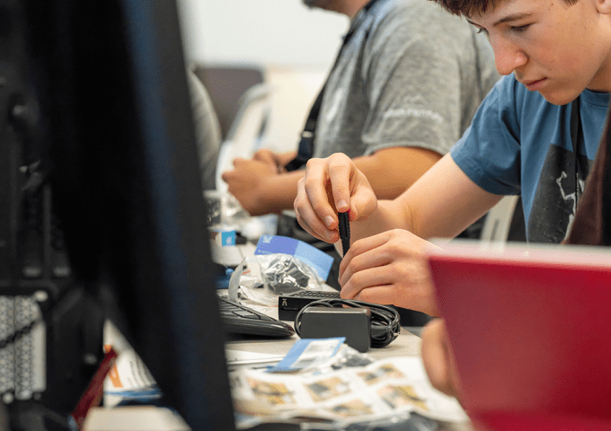 High schooler working on computer hardware using tools.