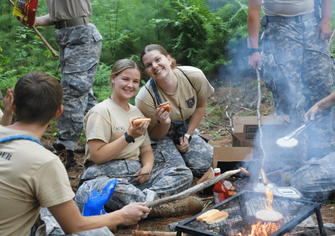 Future Leader Camp attendees in the woods smiling together next to a campfire.