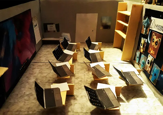 Architectural model of a computer lab with desks, laptops, a large screen, shelves, and colorful wall art.