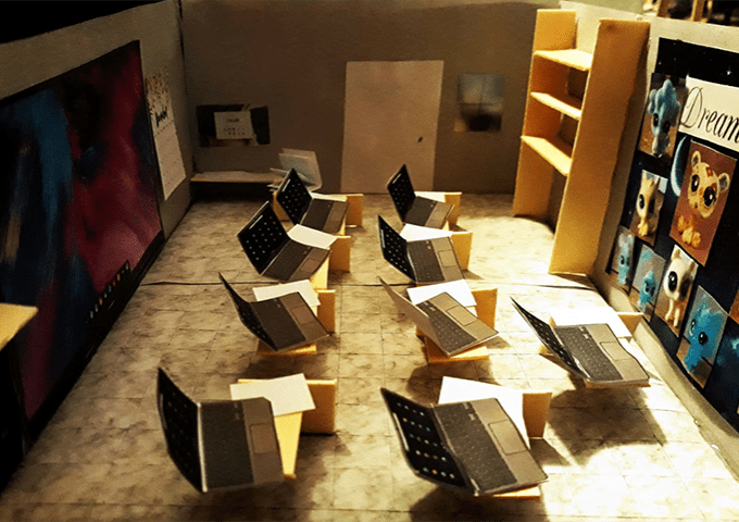 Architectural model of a computer lab with desks, laptops, a large screen, shelves, and colorful wall art.