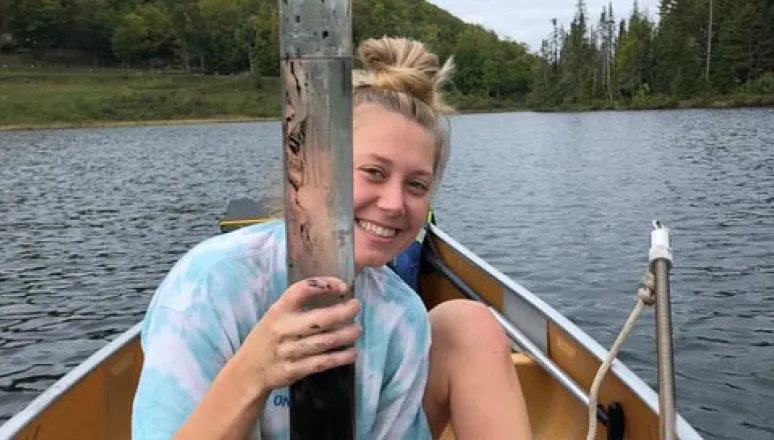 Student in canoe on lake holding a piece of equipment to study the soil.
