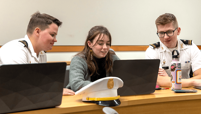 Three students working together on their laptops. Two are in the Corps and one civilian.