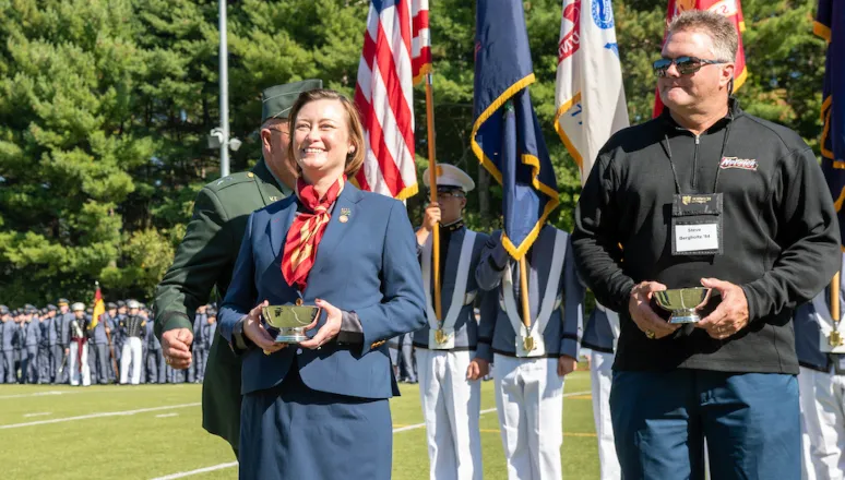 women and man stand on football field holding awards: Dawn Robinson '99 (L), Steven Bergholtz '84 (R)