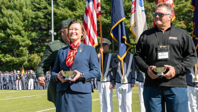 women and man stand on football field holding awards: Dawn Robinson '99 (L), Steven Bergholtz '84 (R)