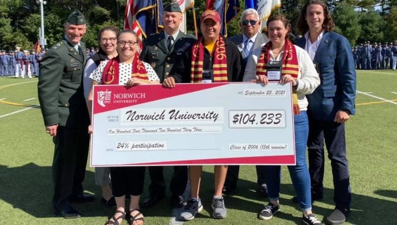 Group of individuals stand on a football field, with three of group holding a large sign in the form of a payment check.