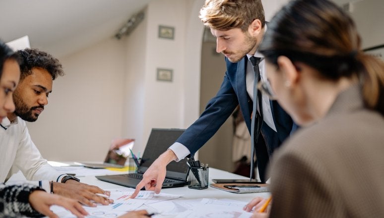 People review printed charts and documents around a conference table while one person points to a report.