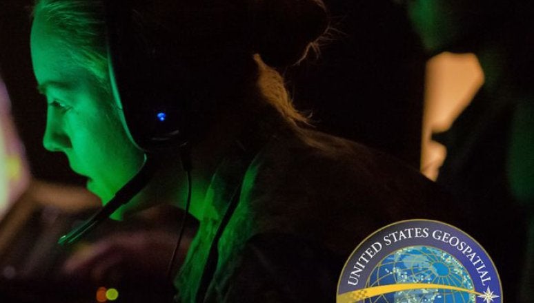 Person wearing a headset uses a computer in a dim room with the Norwich University Go Beyond and USGIF logos visible.