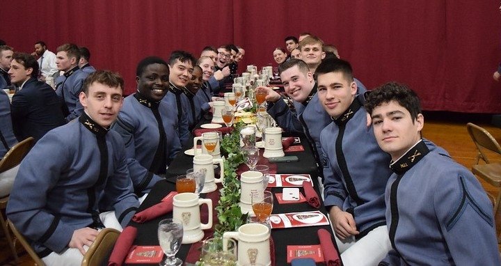 Group of cadets in uniform sitting at a banquet table, smiling at the camera during an event.