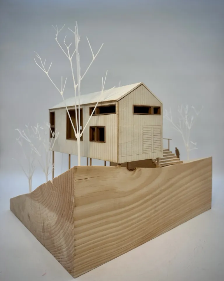 Architectural model of a modern house surrounded by bare trees, displayed on a wooden base.
