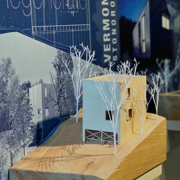 Architectural model featuring a detailed scale model of a building surrounded by miniature white trees on a wooden base.