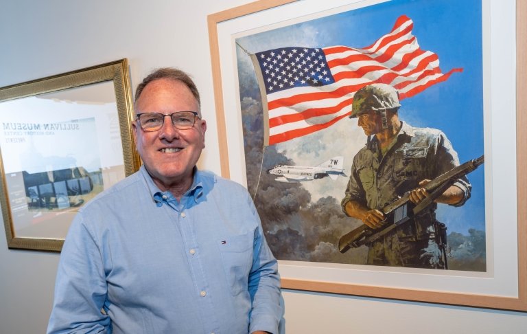 Person smiling and standing in front of a painting depicting a soldier with the American flag in the background.