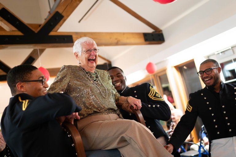 A group of cadets lift an elderly woman in her chair during the Mayo Ball.