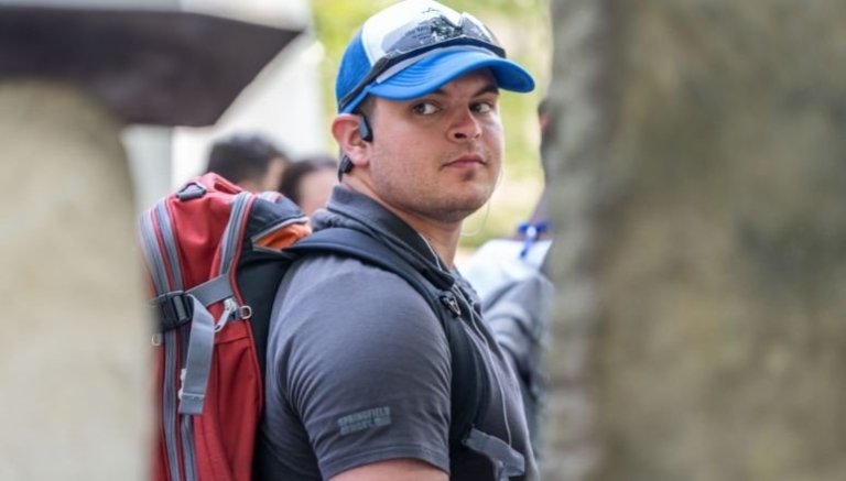 Jayden LaVecchia stands with a hat and sunglasses on top, in a polo wearing a backpack looking over his right shoulder.