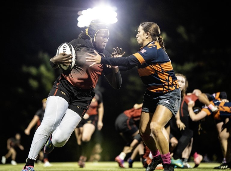 A woman's rugby player runs past a defender with the ball.