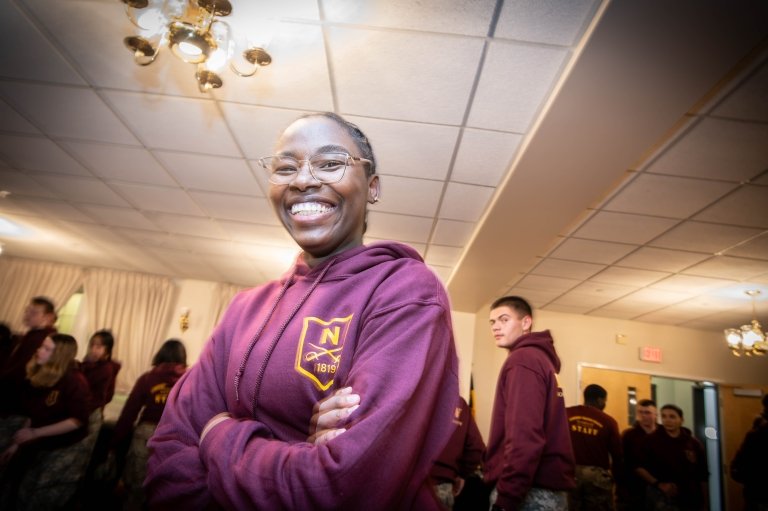 A young woman smiles with her arms crossed in a maroon hoodie.