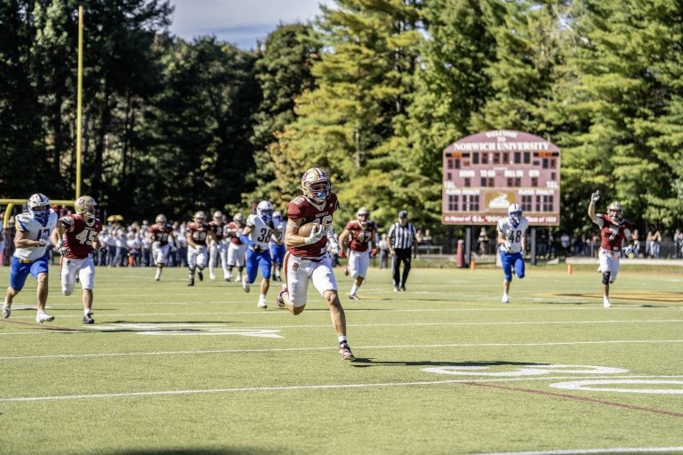 A football player in maroon outruns the defense on his way to a touchdown.