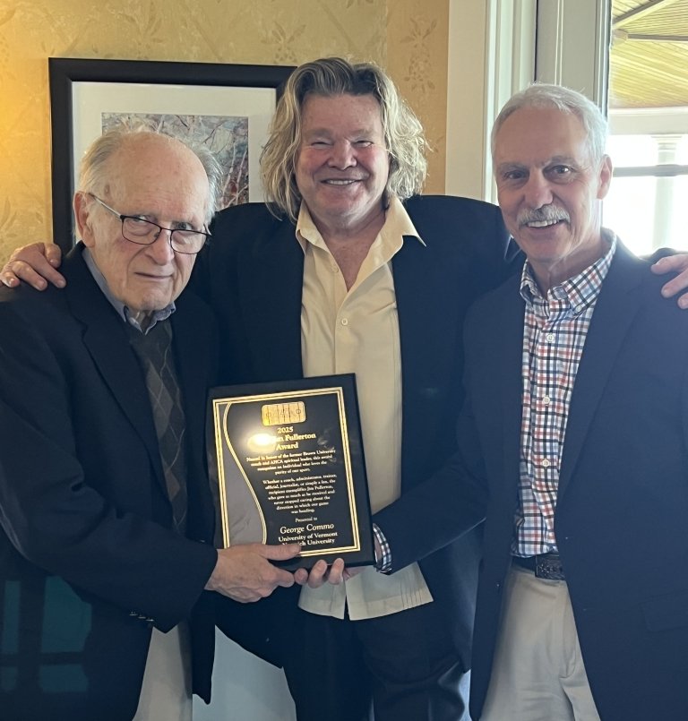Three men hold an award plaque, smiling.
