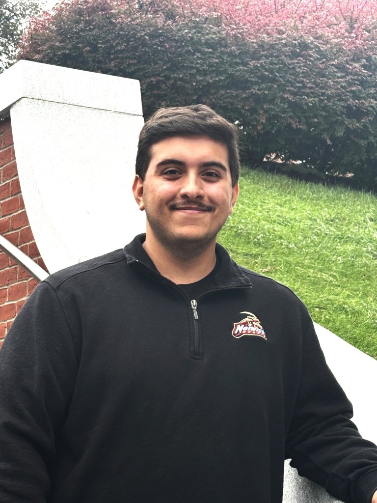A man in a black quarter-zip smiles as he poses on a staircase.