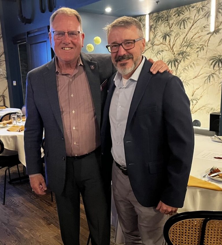 Two men in suits stand smiling.