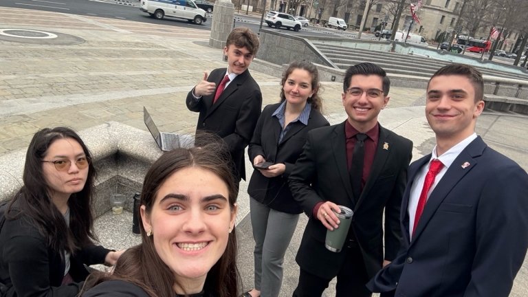 A group of students in formalwear stand together outside on a break from work.