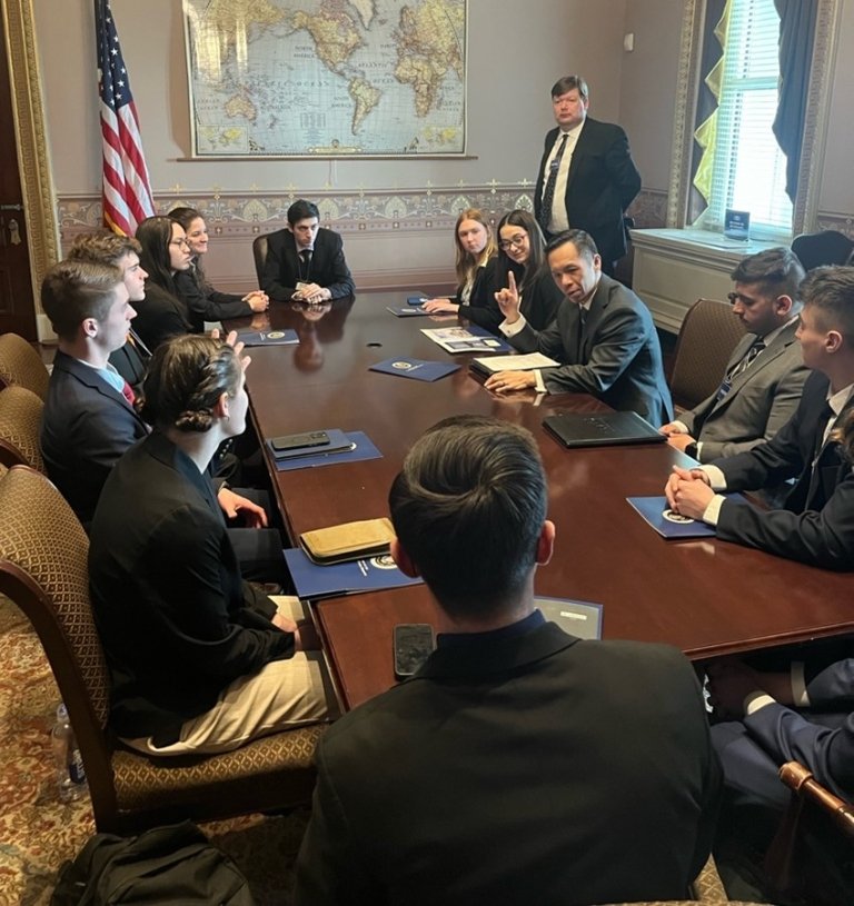 A group of students sit around a meeting table, while an expert talks with them.