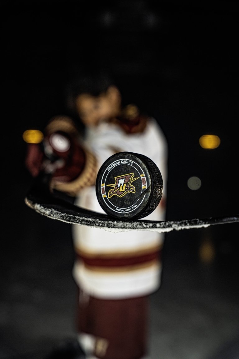 A posed shot of a Norwich hockey player holding a puck on his stick.