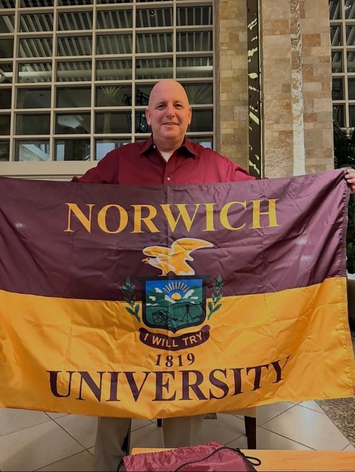 A man smiles as he holds a Norwich flag.