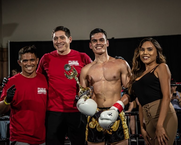 A fighter and his coaches celebrate a victory with a trophy.