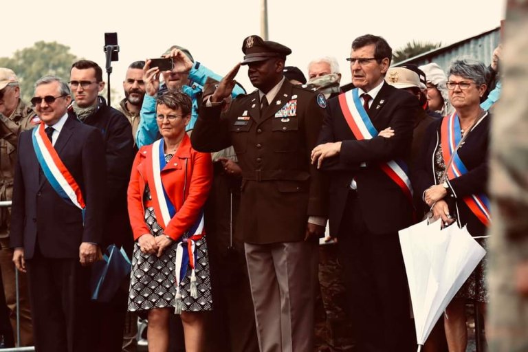 A group of political figures stand around an Army officer, who is saluting.