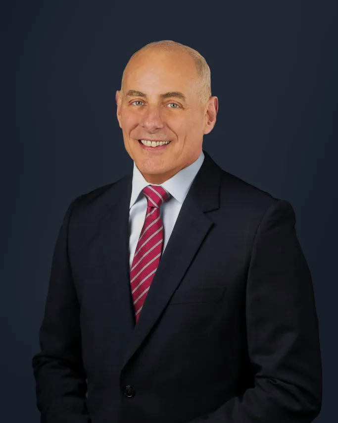 Person wearing a dark suit and red striped tie, smiling against a solid dark background.