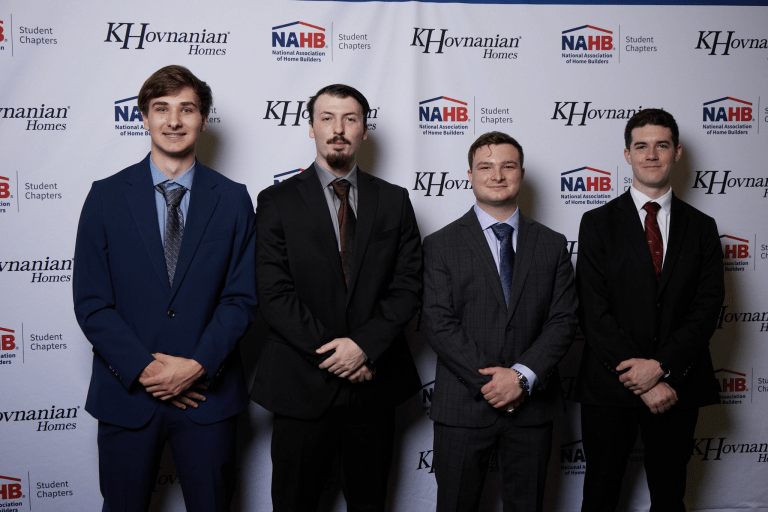 Four people in suits stand in front of a backdrop with KHovnanian Homes and NAHB Student Chapters logos.