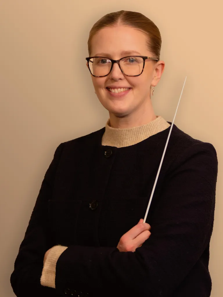 Person in a dark jacket holds a thin baton against a plain background.
