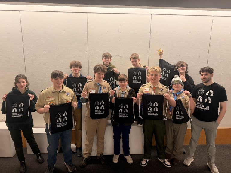 Group of people stand in two rows holding black drawstring bags with white designs in a room with light-colored walls.