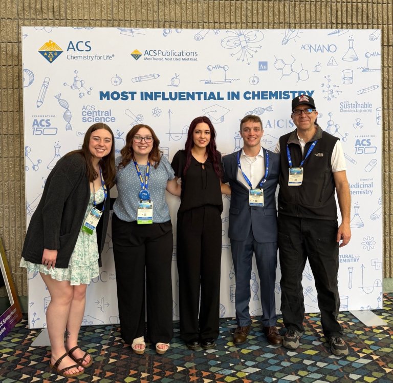 Five people pose with conference badges in front of an ACS Chemistry for Life backdrop.