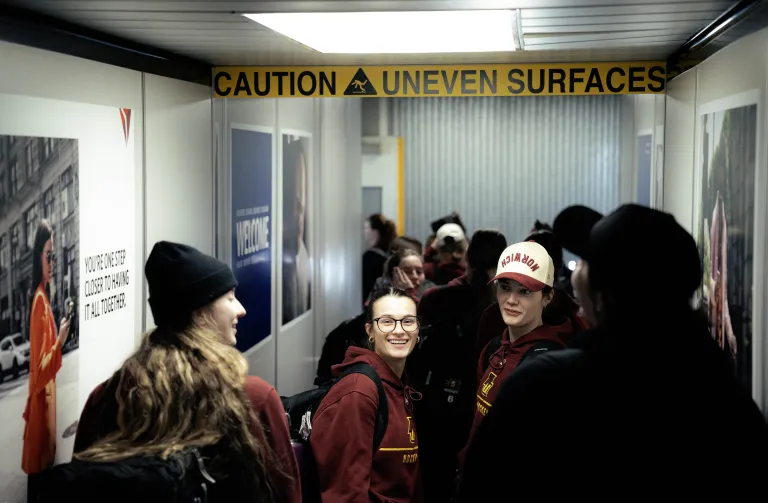 Students in Norwich hockey hoodies walk through a jet bridge beneath a caution uneven surface sign.