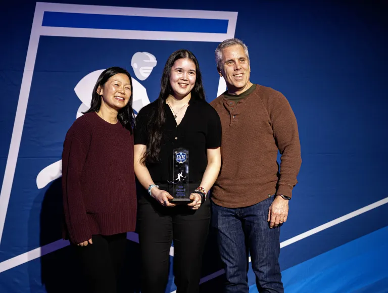 Three people pose with an Elite ice hockey award in front of a blue hockey banner.