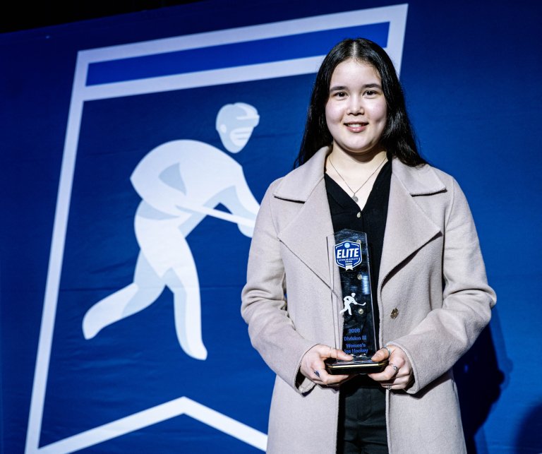 Person holds an Elite award in front of a blue ice hockey banner.