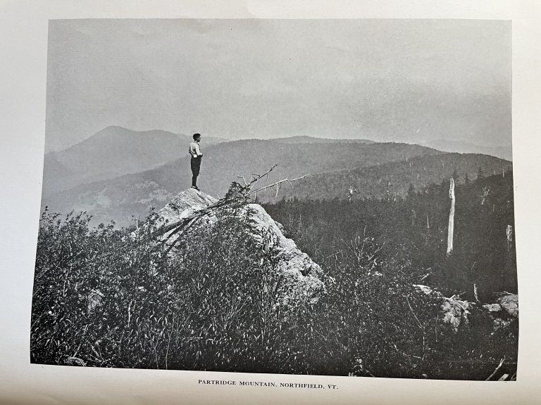 A person stands on a rocky ledge above Partridge Mountain in Northfield, Vermont.