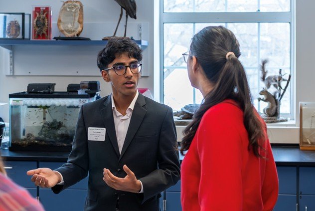 Student in a suit speaks with another person in a classroom.