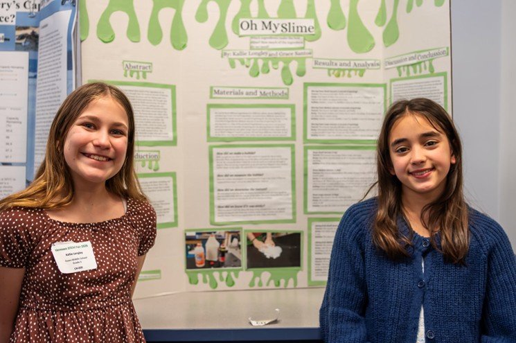 Two students stand in front of a science fair poster titled Oh My Slime.