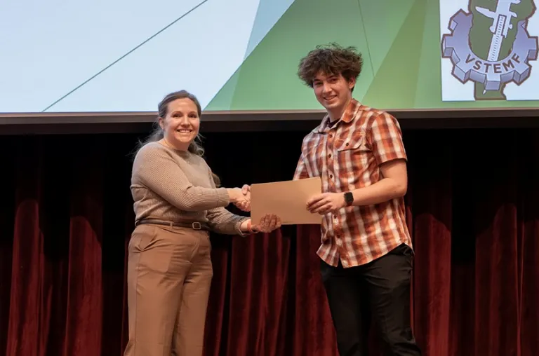 Person shakes hands with a student holding a certificate on a stage.