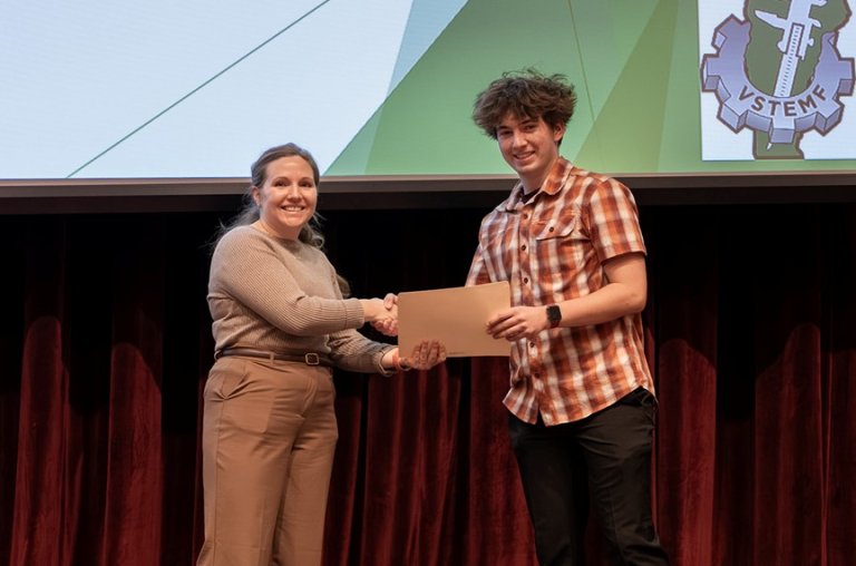 Person shakes hands with a student holding a certificate on a stage.