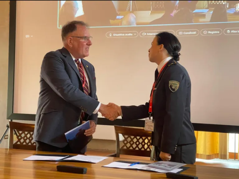 Two people shake hands across a table with papers in a meeting room.
