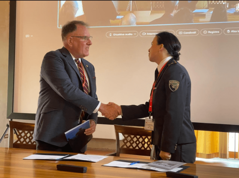 Two people shake hands across a table with papers in a meeting room.